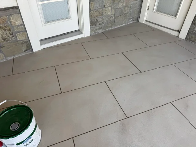 Gray concrete patio coating with running bond pattern and grout lines, adjacent to white doors and stone walls