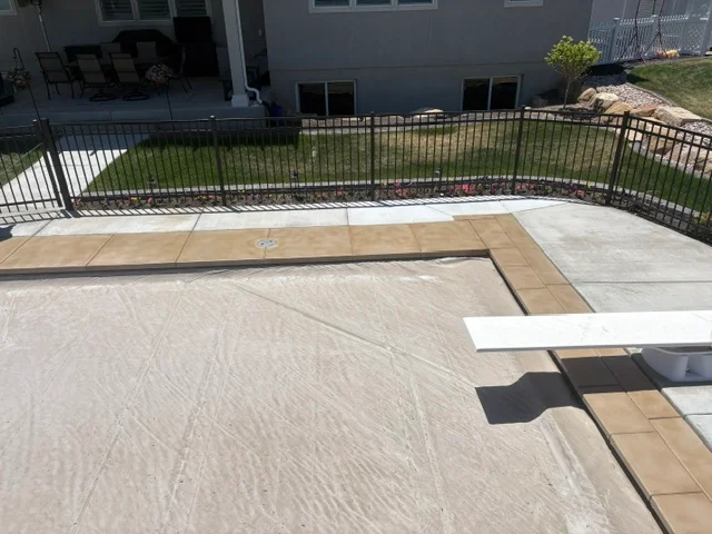 Textured deck coating with wood-grain finish and tan border strips on residential patio with black aluminum railing