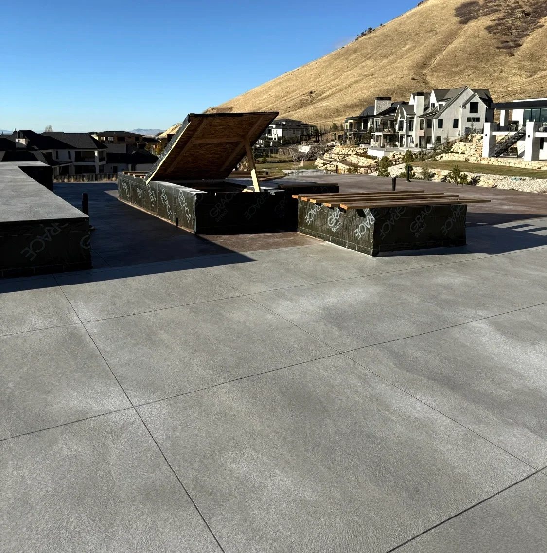 Gray concrete plaza with black metal planters and seating, precision joint lines visible