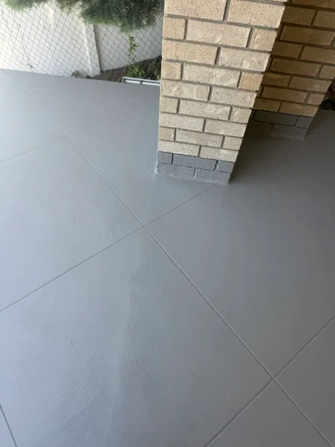 Gray concrete patio coating with clean grout lines and brick foundation