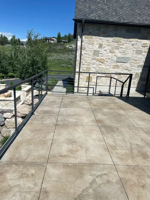 Concrete deck with scored coating pattern, black metal railings, stone veneer wall