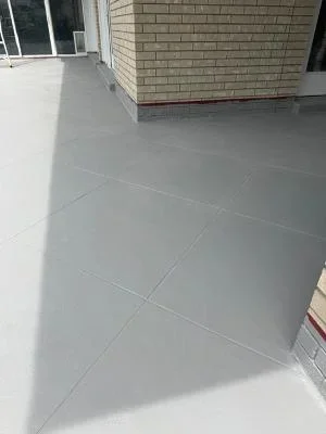 Gray coated deck with large format pavers and clean seams against brick building